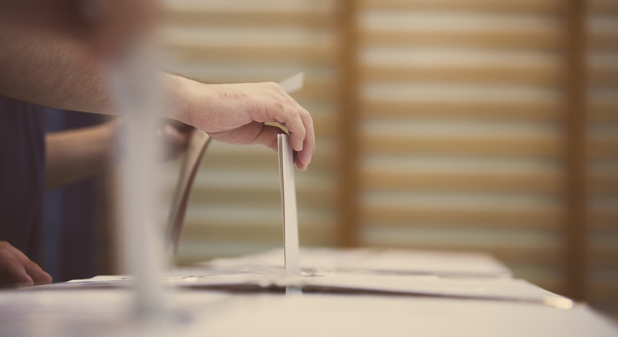 Hand putting a folded paper into a ballot box.
