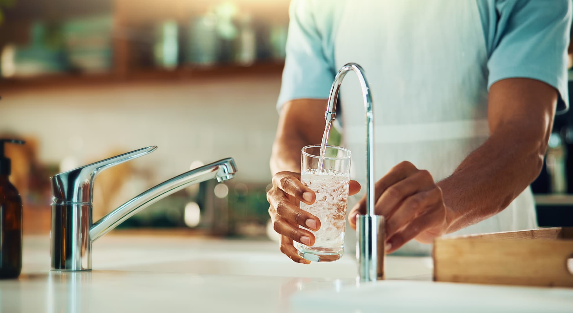 A woman's hand holding a glass of water under a tap.