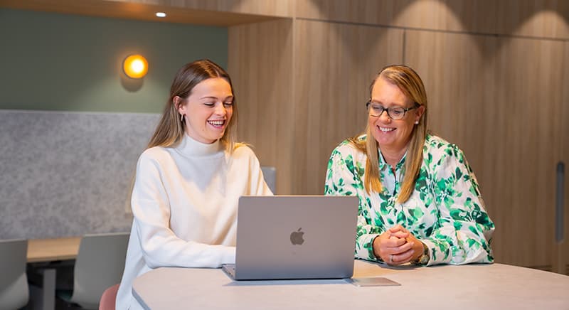 A student and teacher sit at a desk looking at a laptop