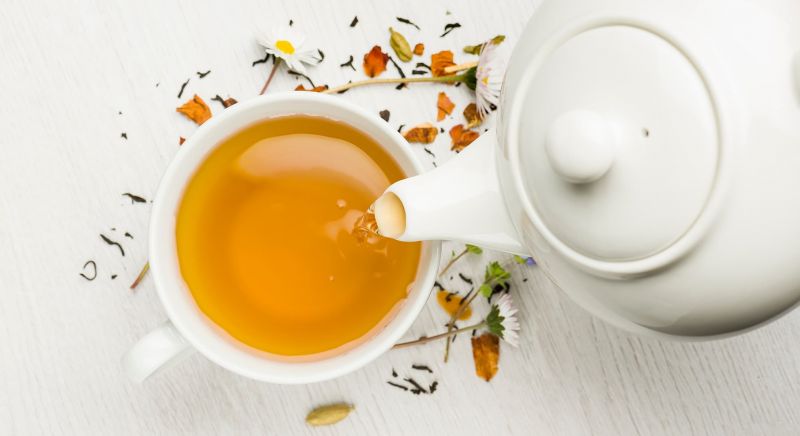 White teapot pouring pale yellow tea into cup.