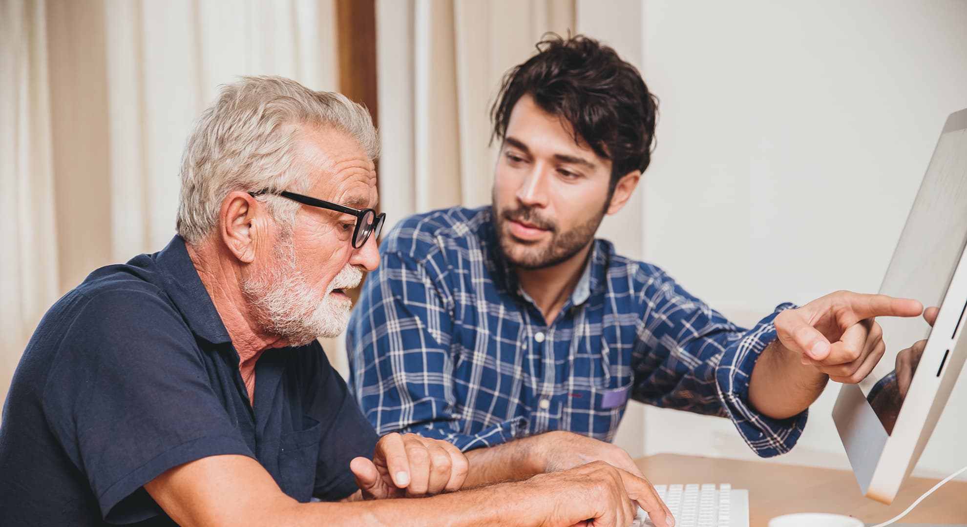 A man pointing to computer screen helping elderly man