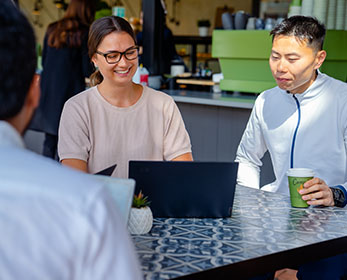 Researchers sit and have a coffee together, one showing the other an item on their laptop screen.