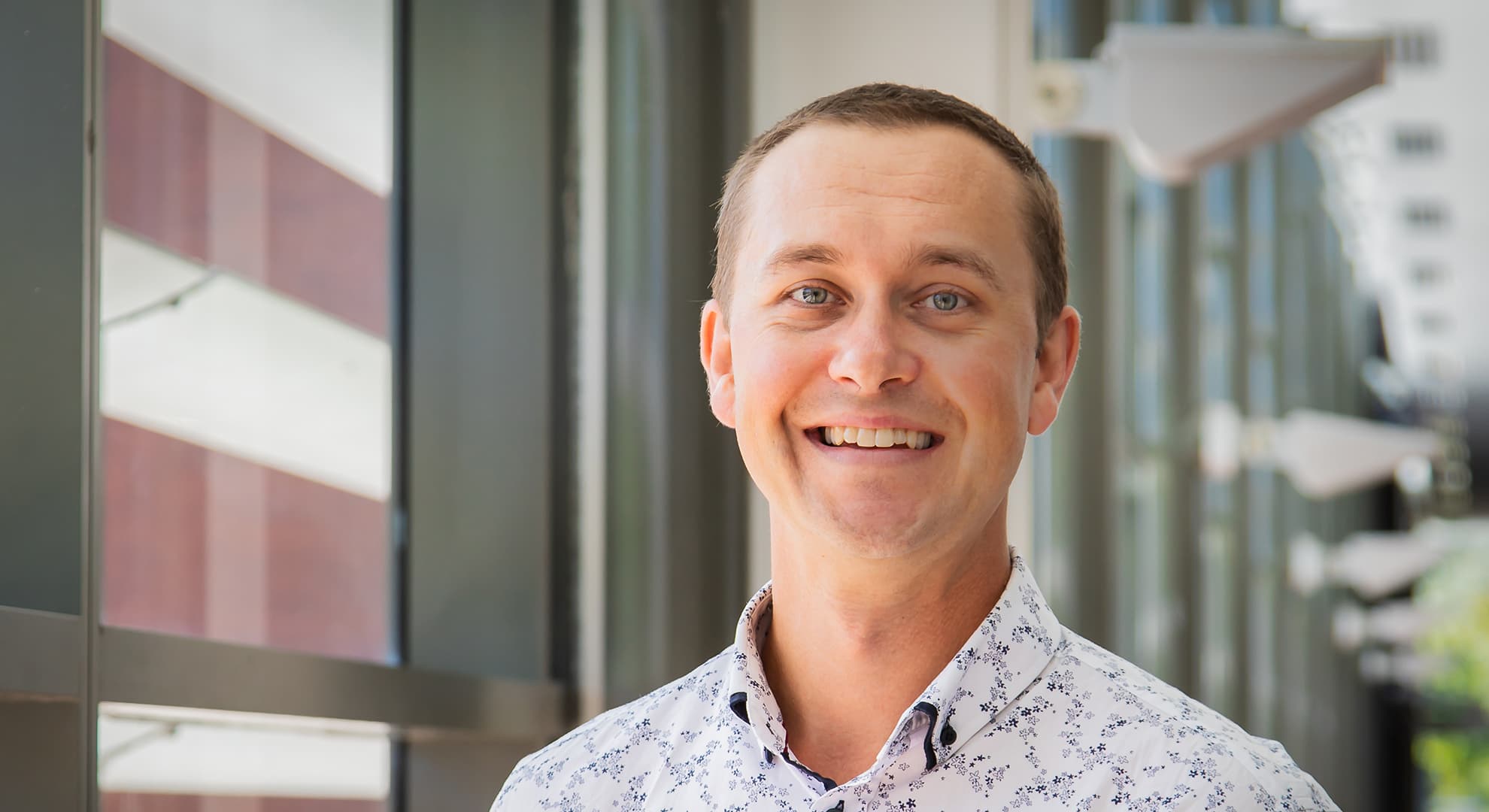 Dr Luke Hopper wears a blue printed button-down shirt and smiles outdoors.