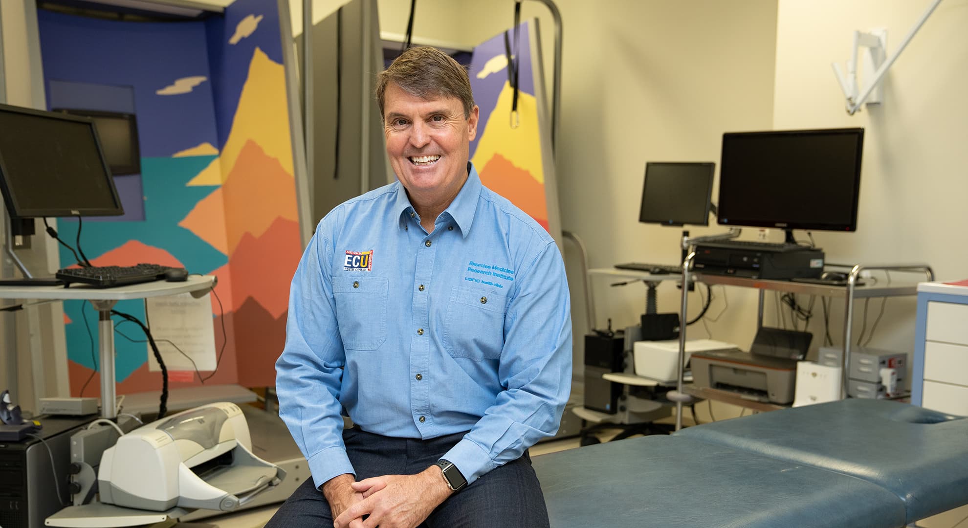 Man sitting on a bed in medical exam room, smiling.