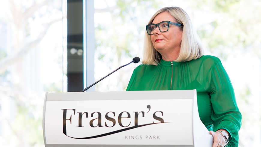 Dr Tania Beament wears a bright green dress and stands at the podium as MC.