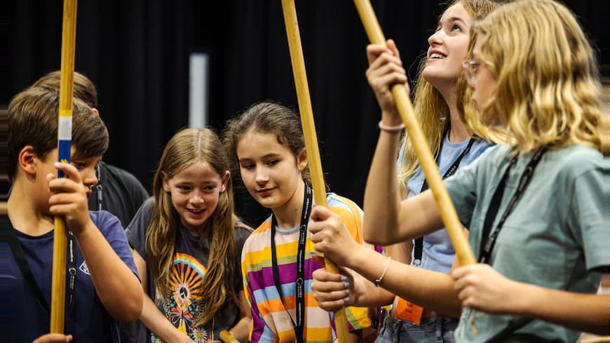 children grouped closely holding long wooden sticks