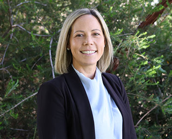 A portrait image of Associate Professor Christine Robinson smiling and staning in front of some trees.