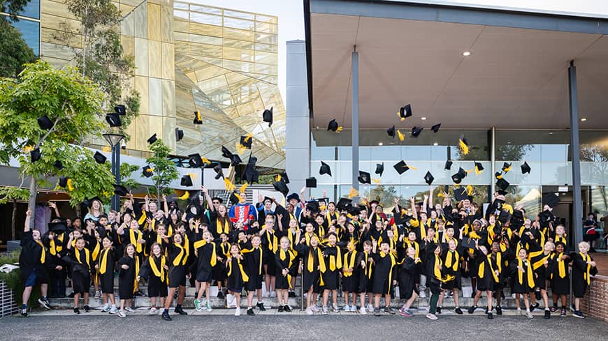 Students and supporters celebrating in their full regalia at the 2025 ECU Children's University WA Graduation, throwing their graduate caps into the air.