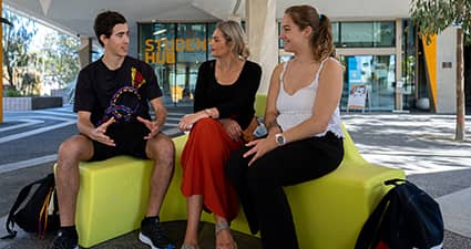 Three students sitting outside the Student Hub