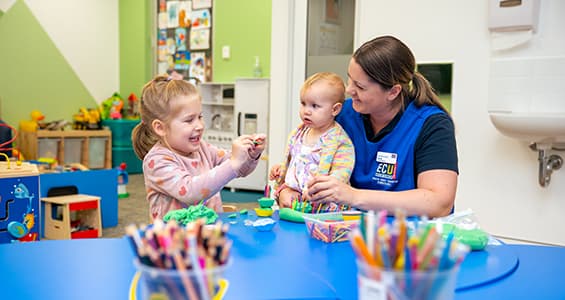 Childcare worker sitting at a small desk with two young children.