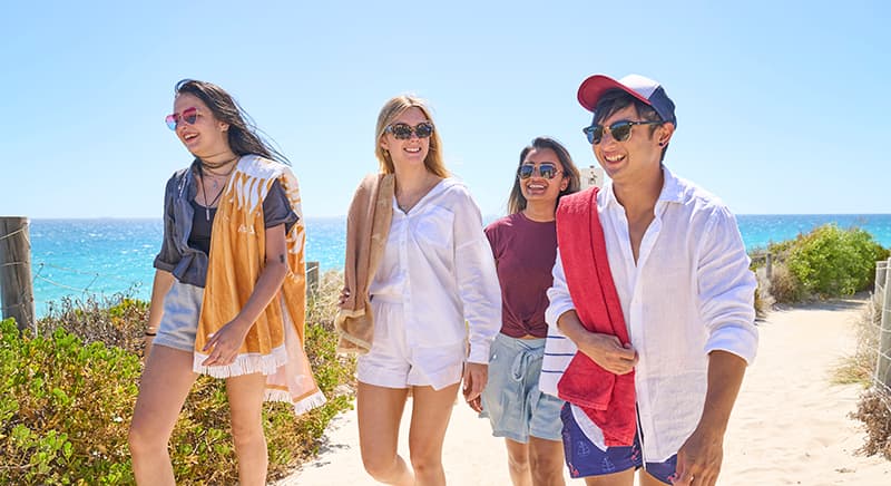 Fours students walking up beach path wearing bright summer clothes.