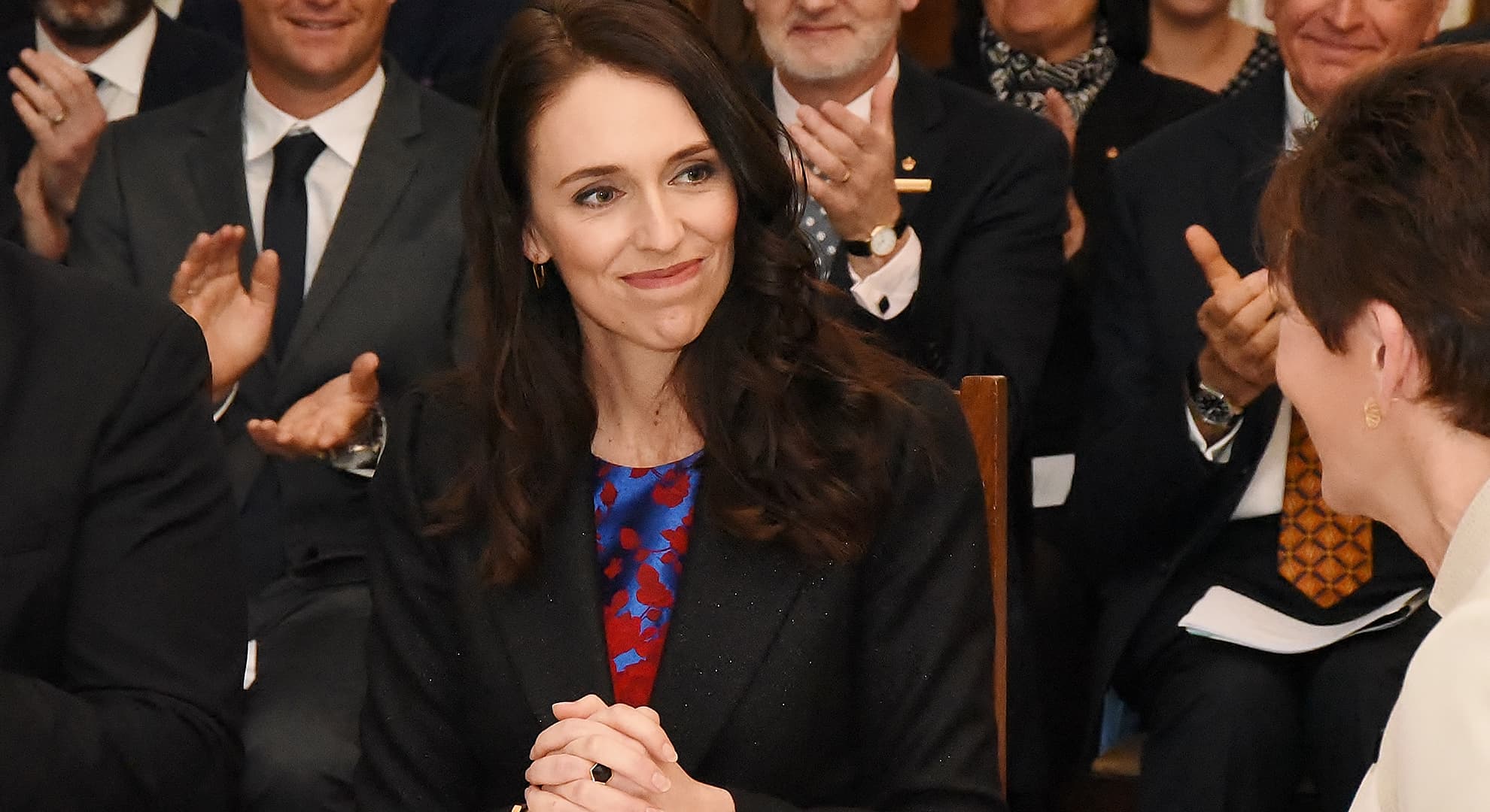 Jacinda Ardern sitting at table surrounded by applauding people as she is sworn in as New Zealand Prime Minister.