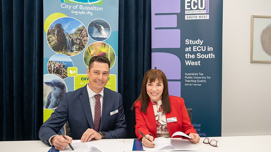 Two people sitting at a desk signing an agreement.