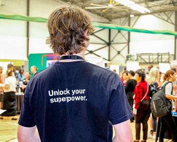 A person standing with their back towards the camera in a crowded room full of people attending a careers fair.