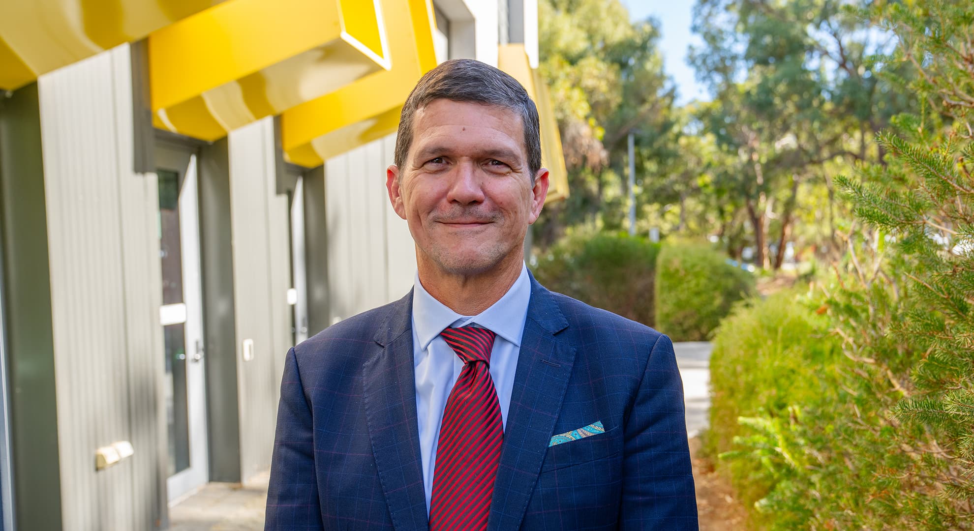 Paulo de Souza wears a blue suit and red tie outdoors on the ECU Joondalup campus.
