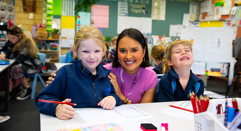 Trainee teacher in classroom, two young children at her side