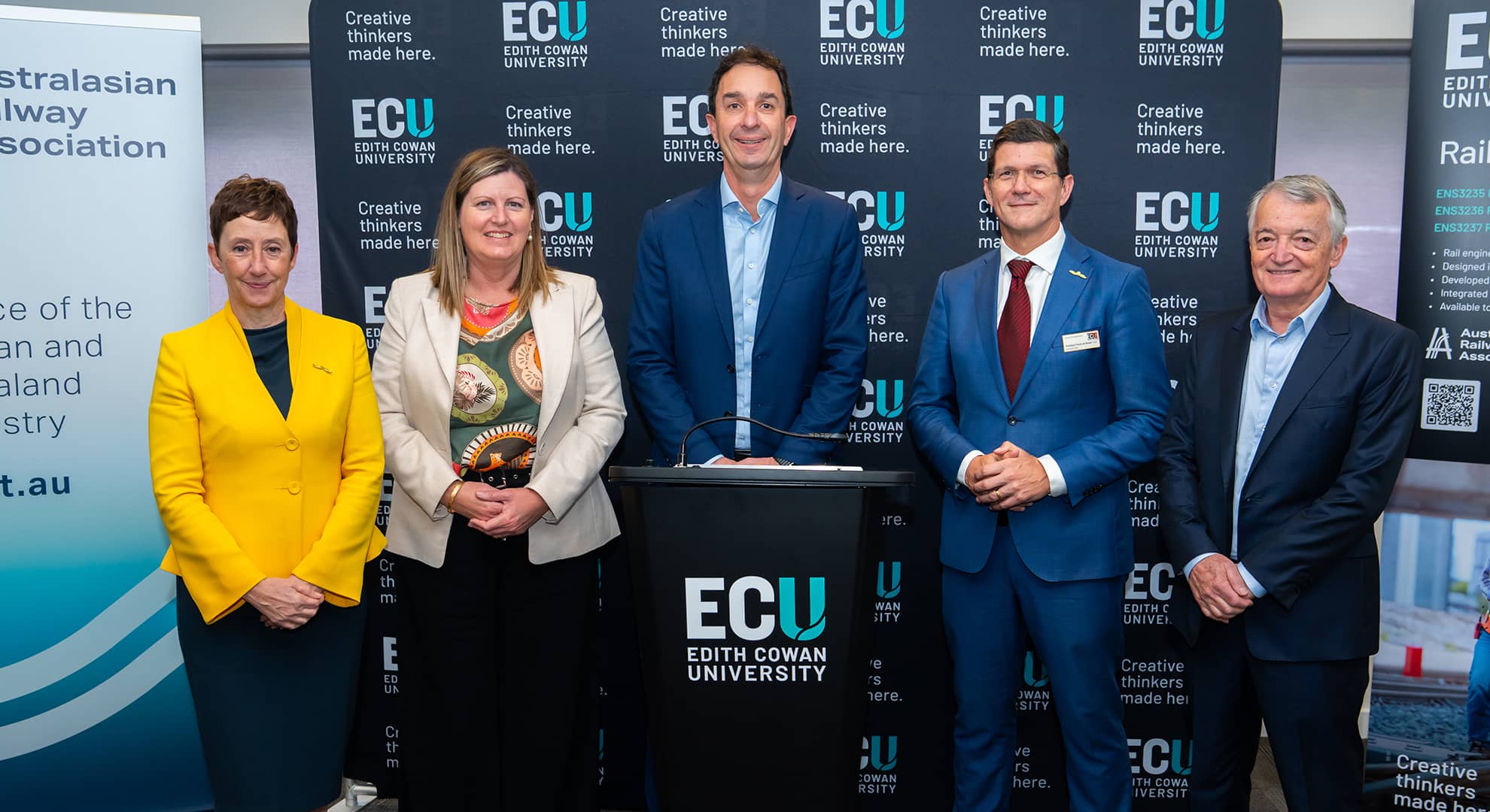 Two women and three men standing behind a podium.
