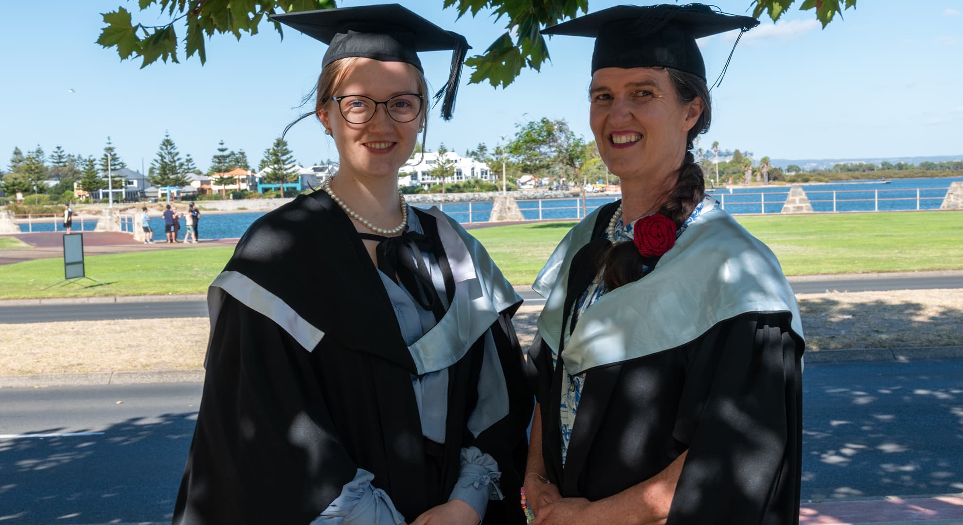 A daughter and mother standing in graduation gowns.