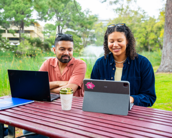 Two students sitting outdoors using laptops and a tablet, accessing digital content through ECU Library