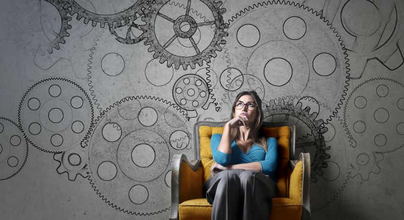 woman leaning against wall decorated with drawings of cogs, thinking