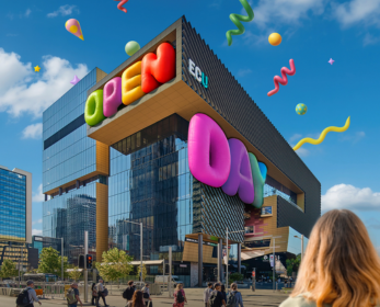 The ECU City Campus building decorated with colourful Open Day graphics, viewed from street level under a blue sky. Pedestrians are crossing the intersection in the foreground, with a visitor looking towards the building from the lower right of the image. Colourful streamers and balloons add a festive atmosphere.