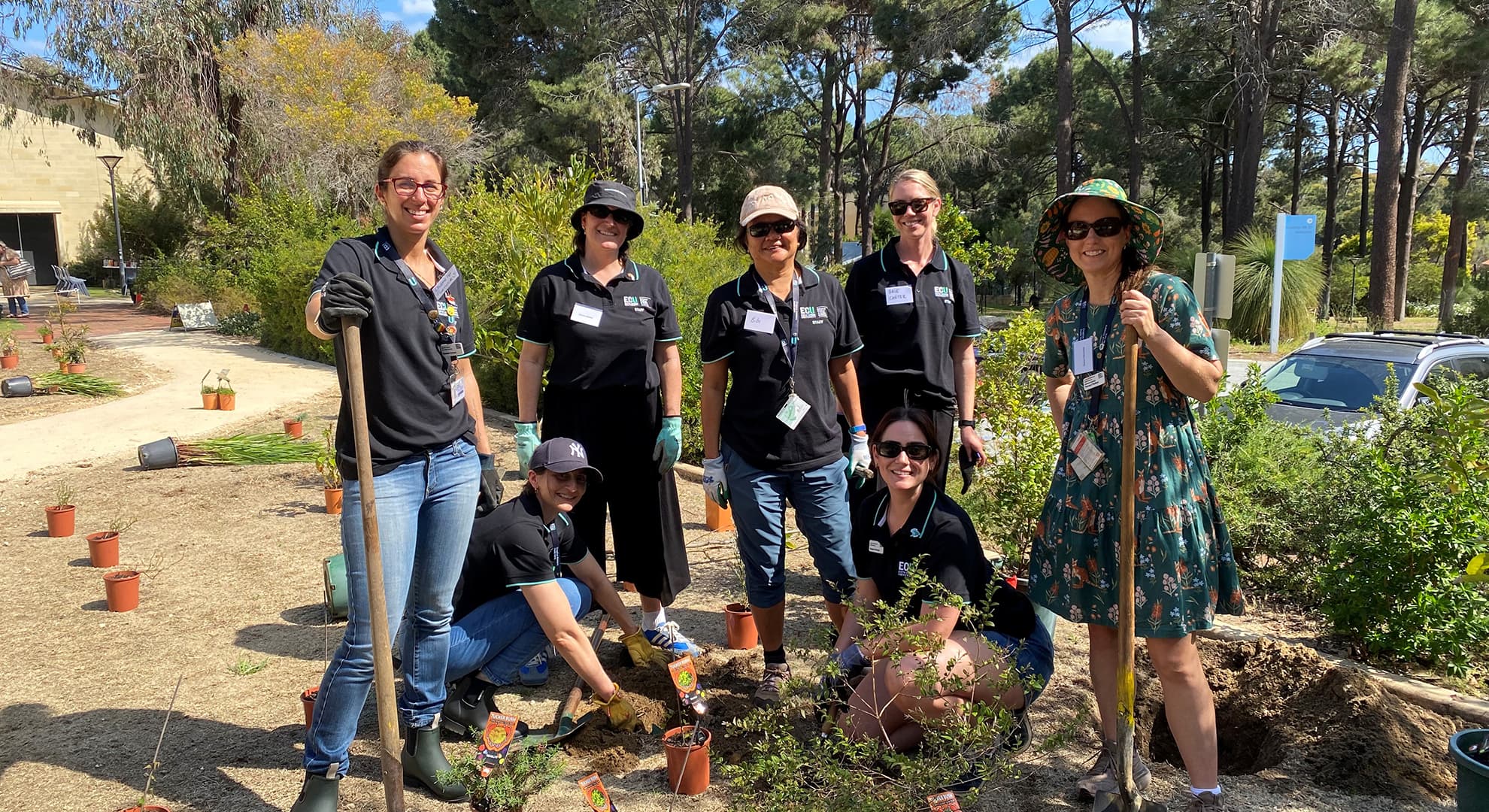 A group of people standing in the garden with spades and plants to be planted.