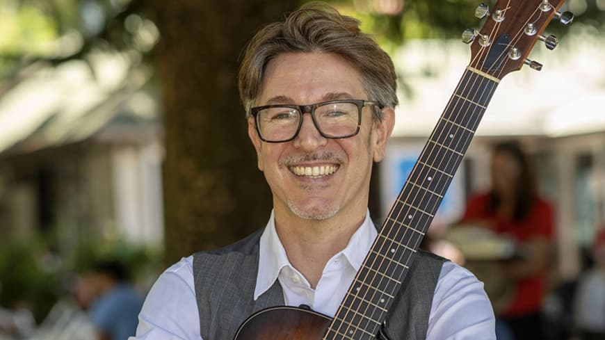 Dr Marino holding a guitar and smiling.