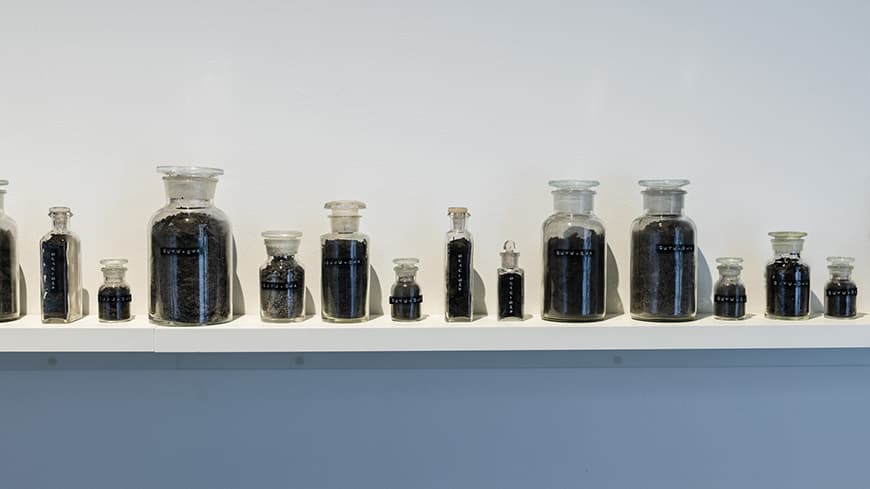 Bottles of black material lined up on a white shelf against a white wall.