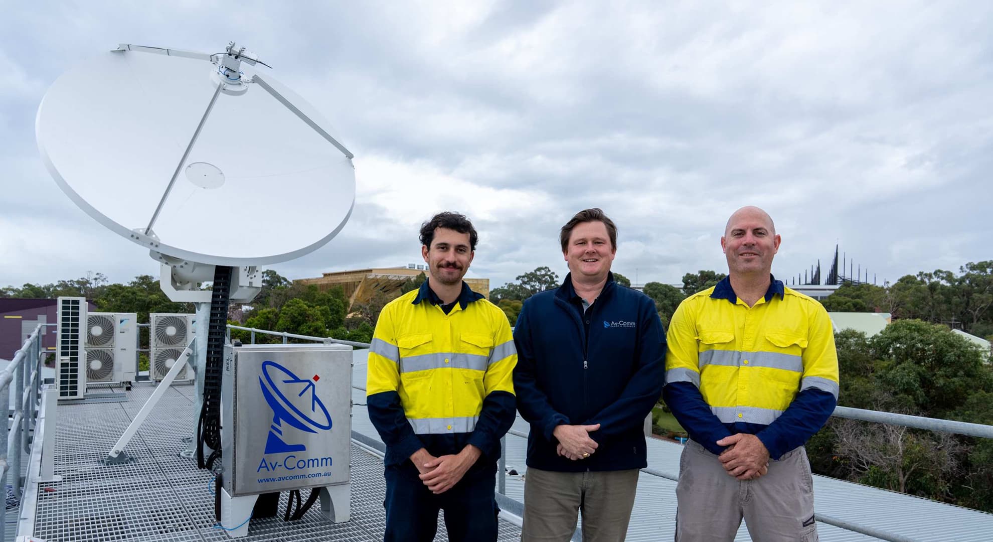 Three men on roof with satellite ground station in background