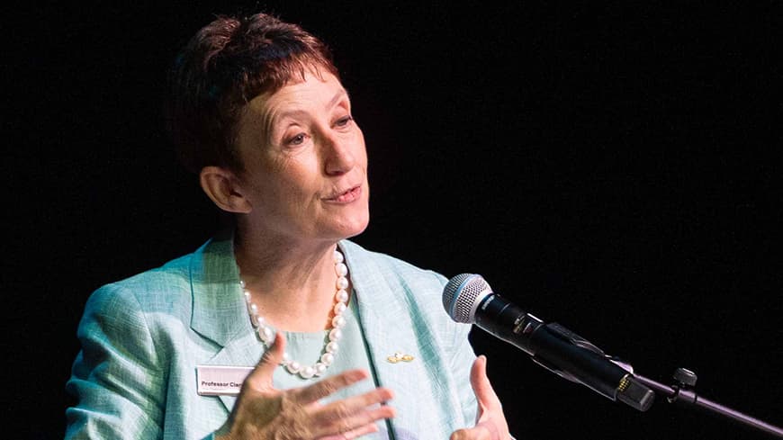 VC Professor Clare Pollock speaking behind a podium at the conference.