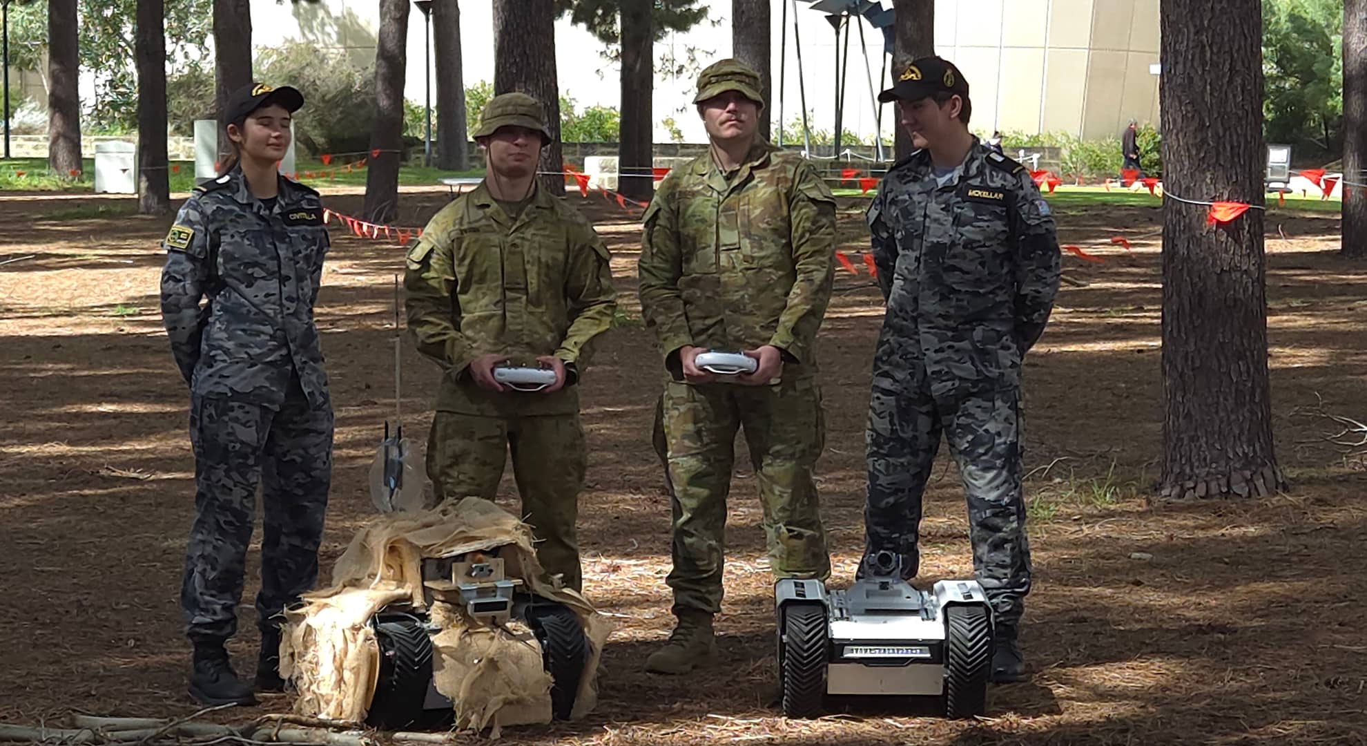 Four soldiers standing in front of two robots.