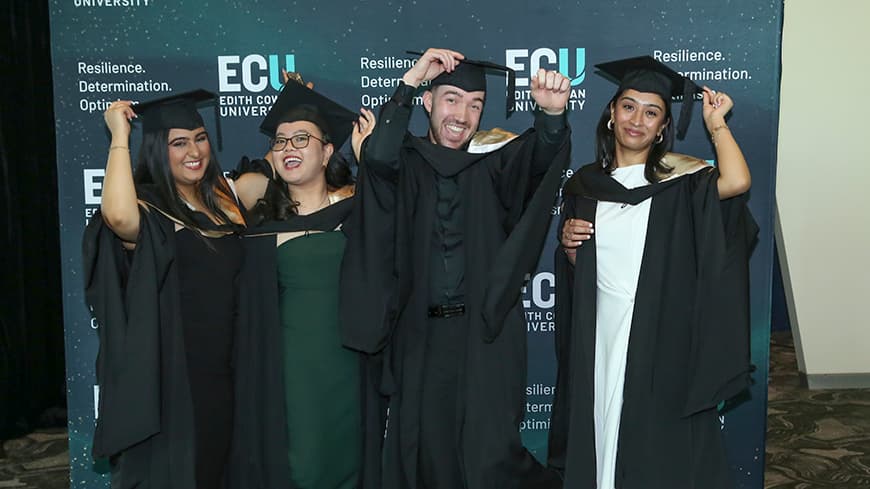 Four graduates posing for the camera, holding their hats