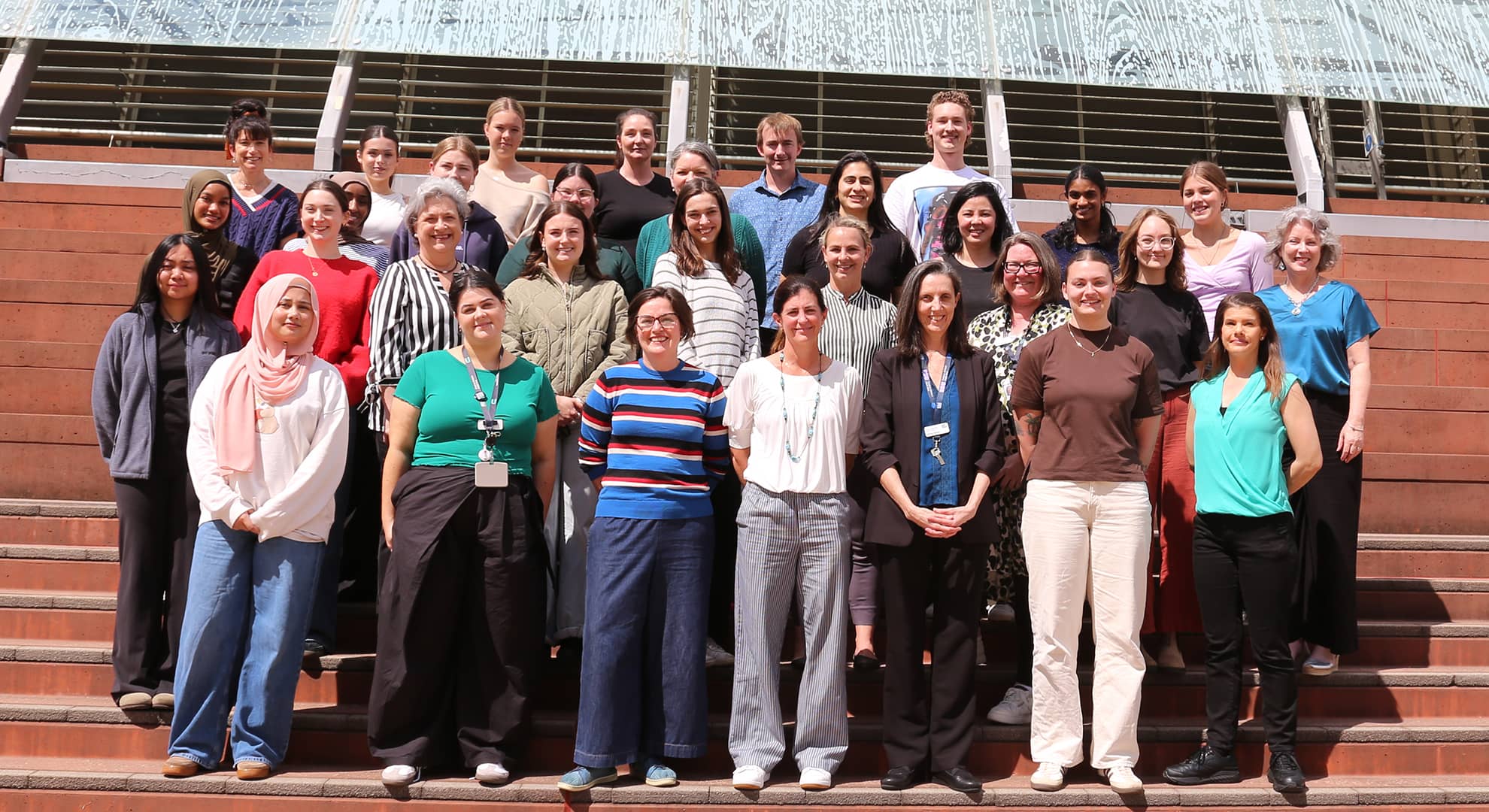 The third year cohort standing on steps squinting in the bright sunlight.