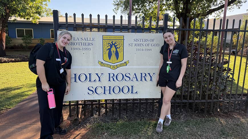 Two female students stand outside a school