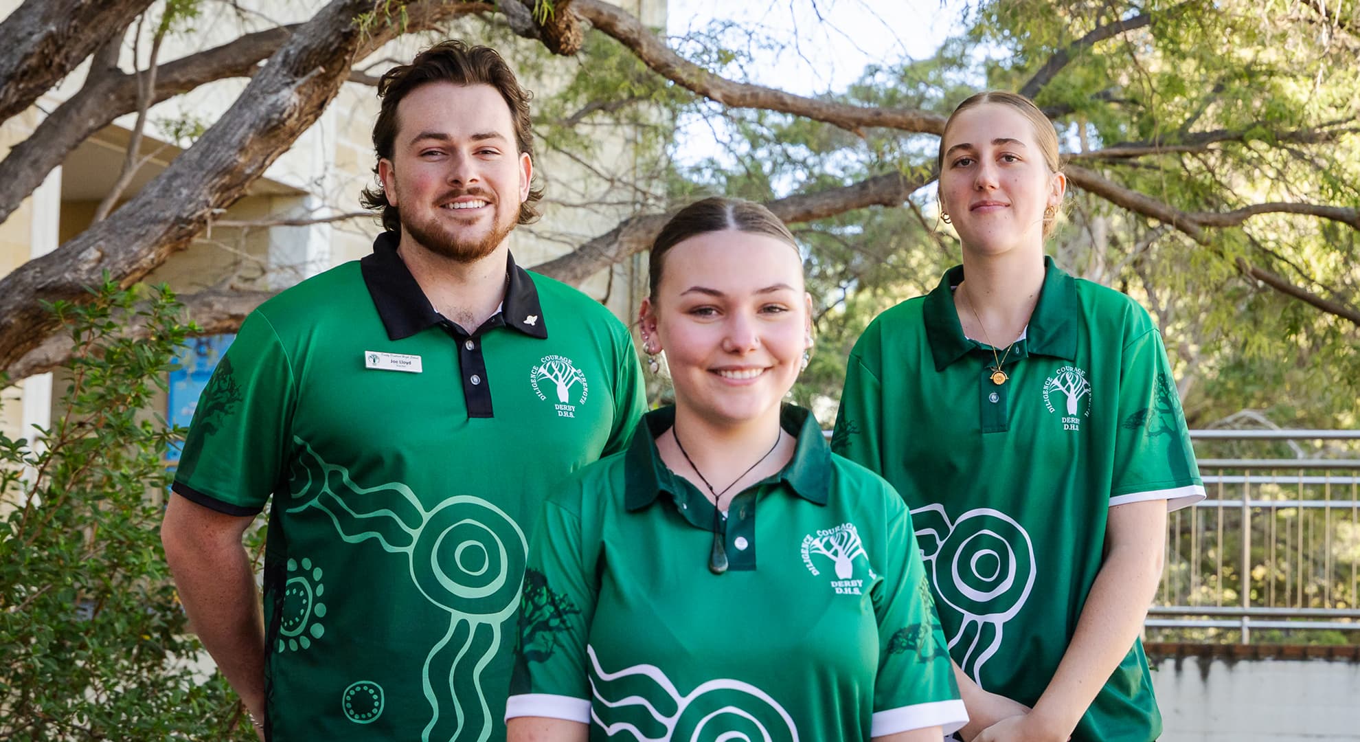 Male teacher and two female students in green school t-shirts