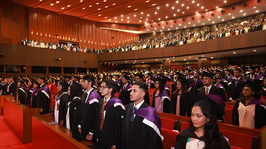 People in graduation regalia, standing in formal seating arrangements.
