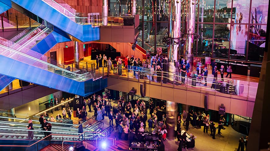 A wide image showing lots of people inside a building.