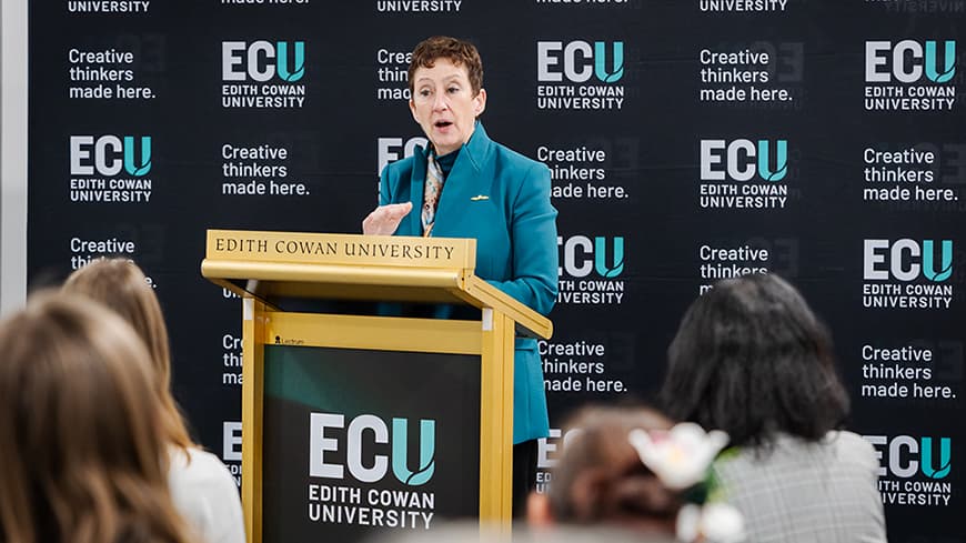 Woman at a lectern talking to a crowd of people seated
