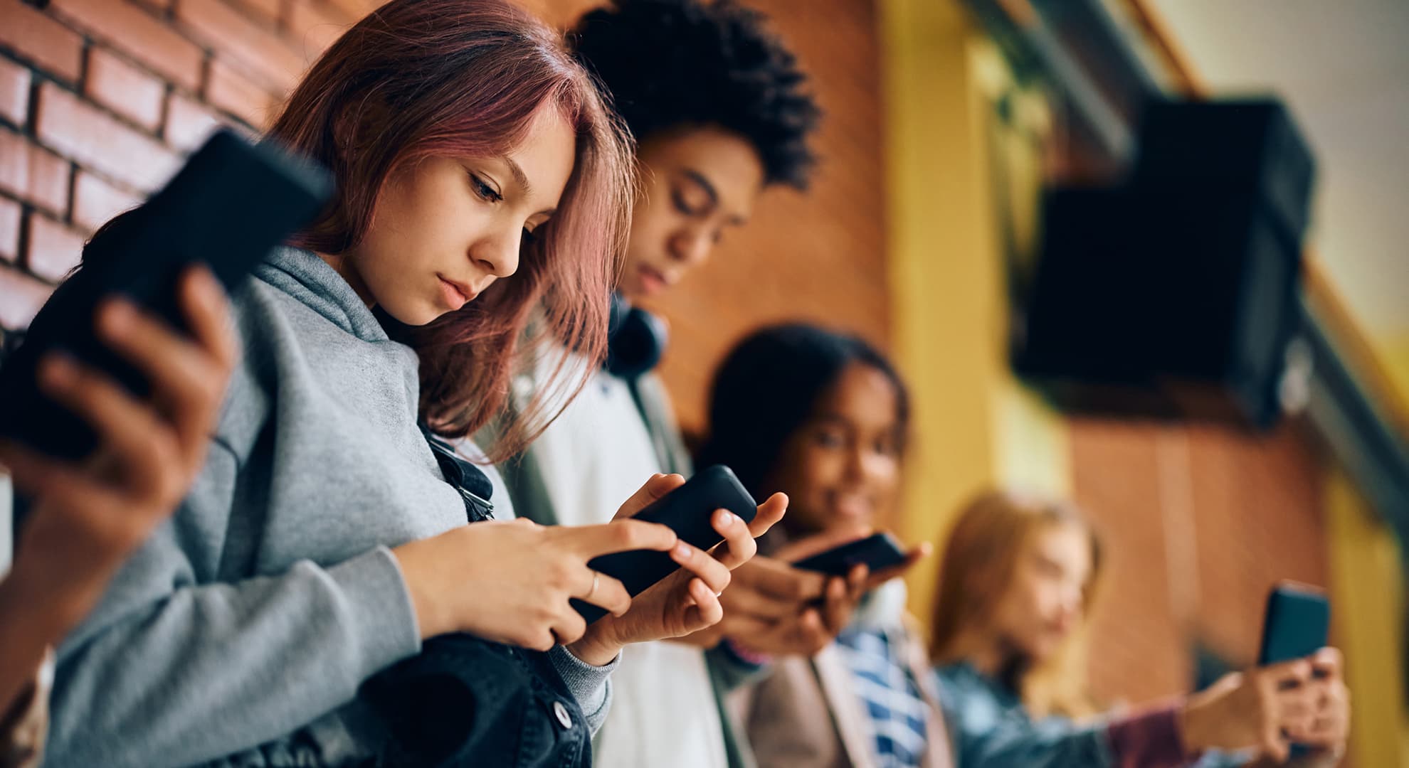 High school student and her friends using their smart phones in a hallway.