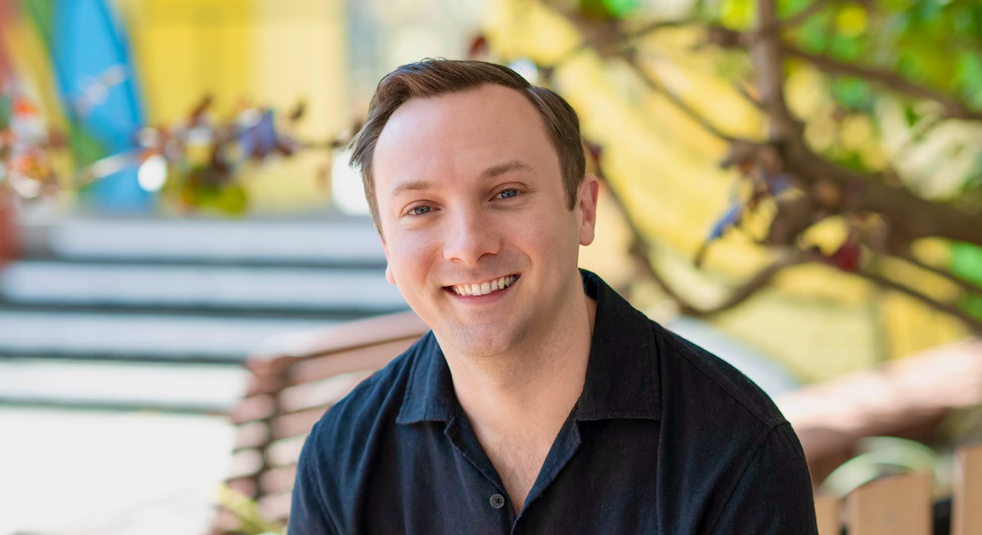 Scott Elstermann sitting and smiling happily in the sunshine outside ECU City Campus
