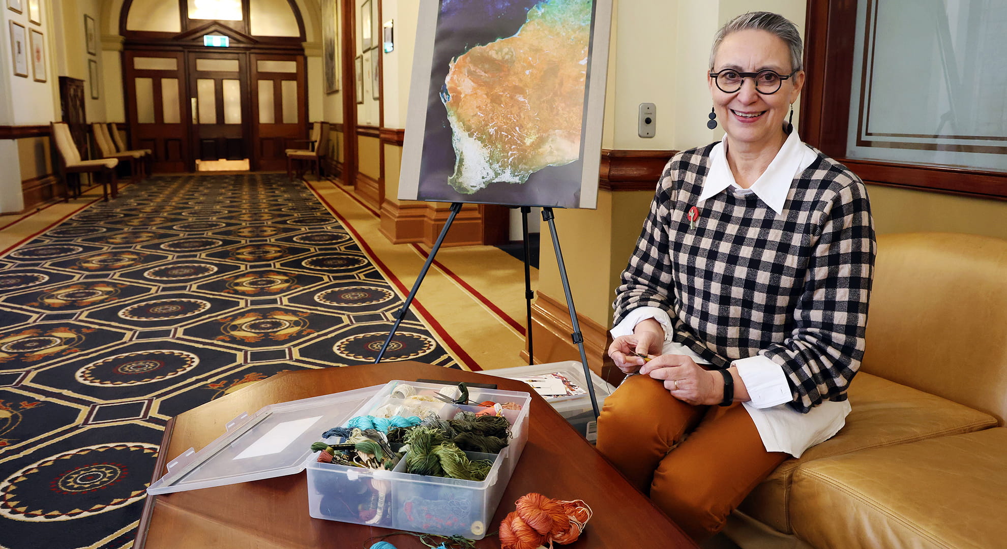 A woman sitting with artist wool and a map of WA in the background.