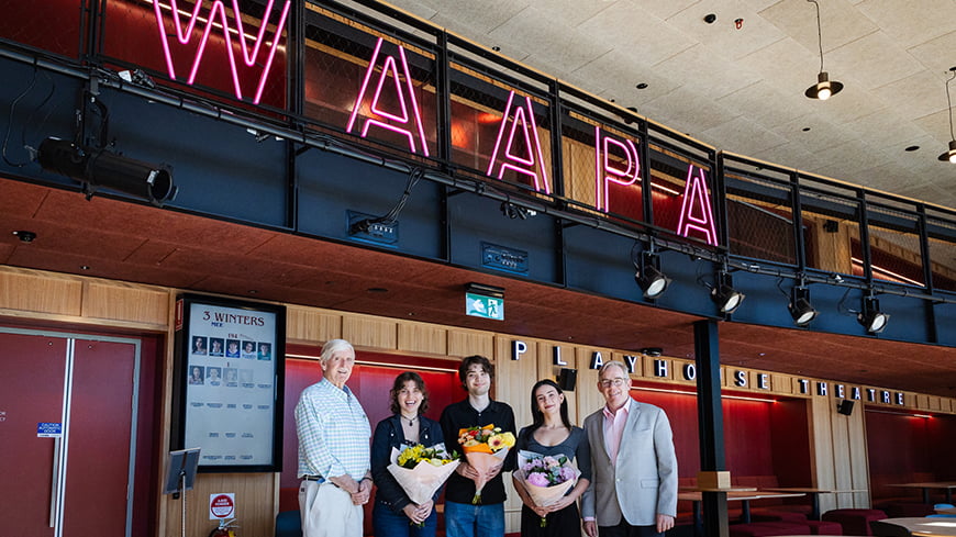 A group of five people standing indoors, with three holding flowers.