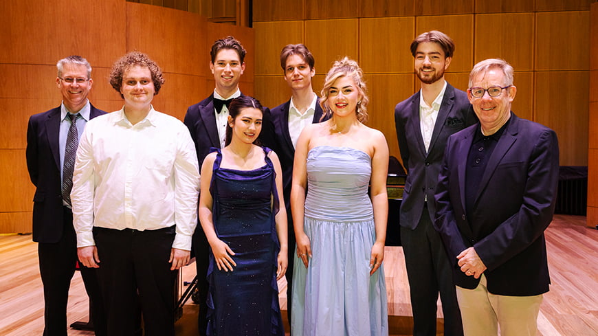 Two women in formal dress standing with six men in suits.