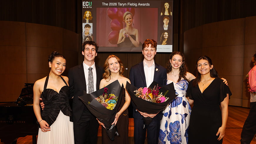 A group of six people smiling, with two holding flowers.