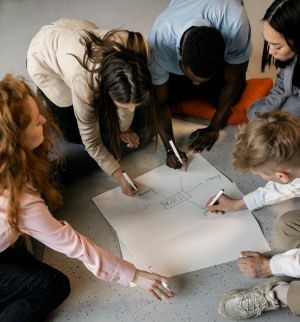 A group of teenagers gather around a large piece of paper to brainmap an idea.