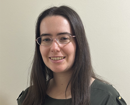 Photo of a young woman with straight dark brown hair and glasses, wearing a green top