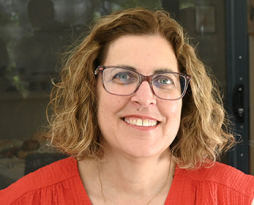 Headshot of a woman with brown hair, glasses and an orange top