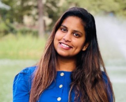 Photo of a woman with long dark hair with a blue blouse in front of a lake 