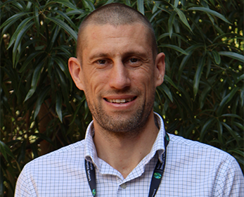 Photo of a man with short cropped hear wearing a blue check shirt