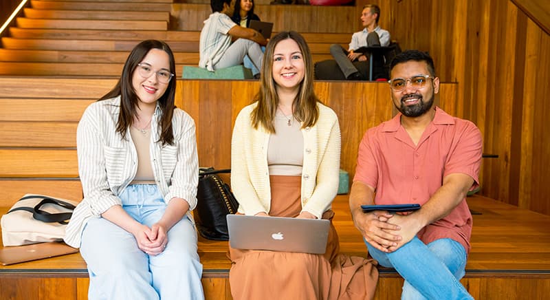 Three students sitting on steps smiling for the camera